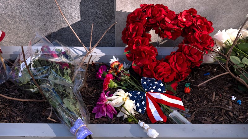 Un pequeño monumento hecho con banderas, flores y otros objetos en una jardinera, el viernes...